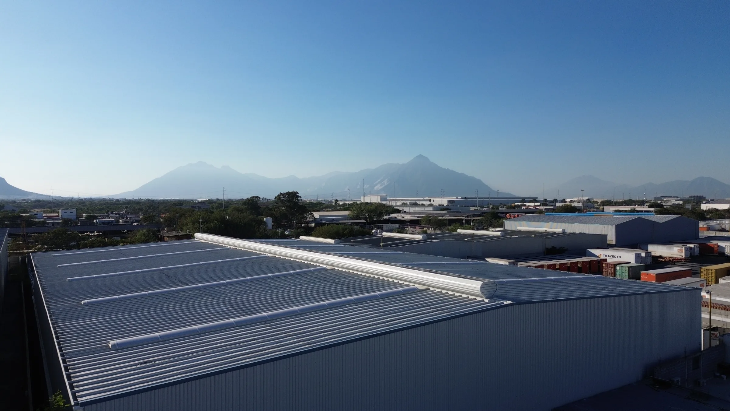 Vista aérea de una nave industrial terminada con domos continuos en el techo y cerros al fondo