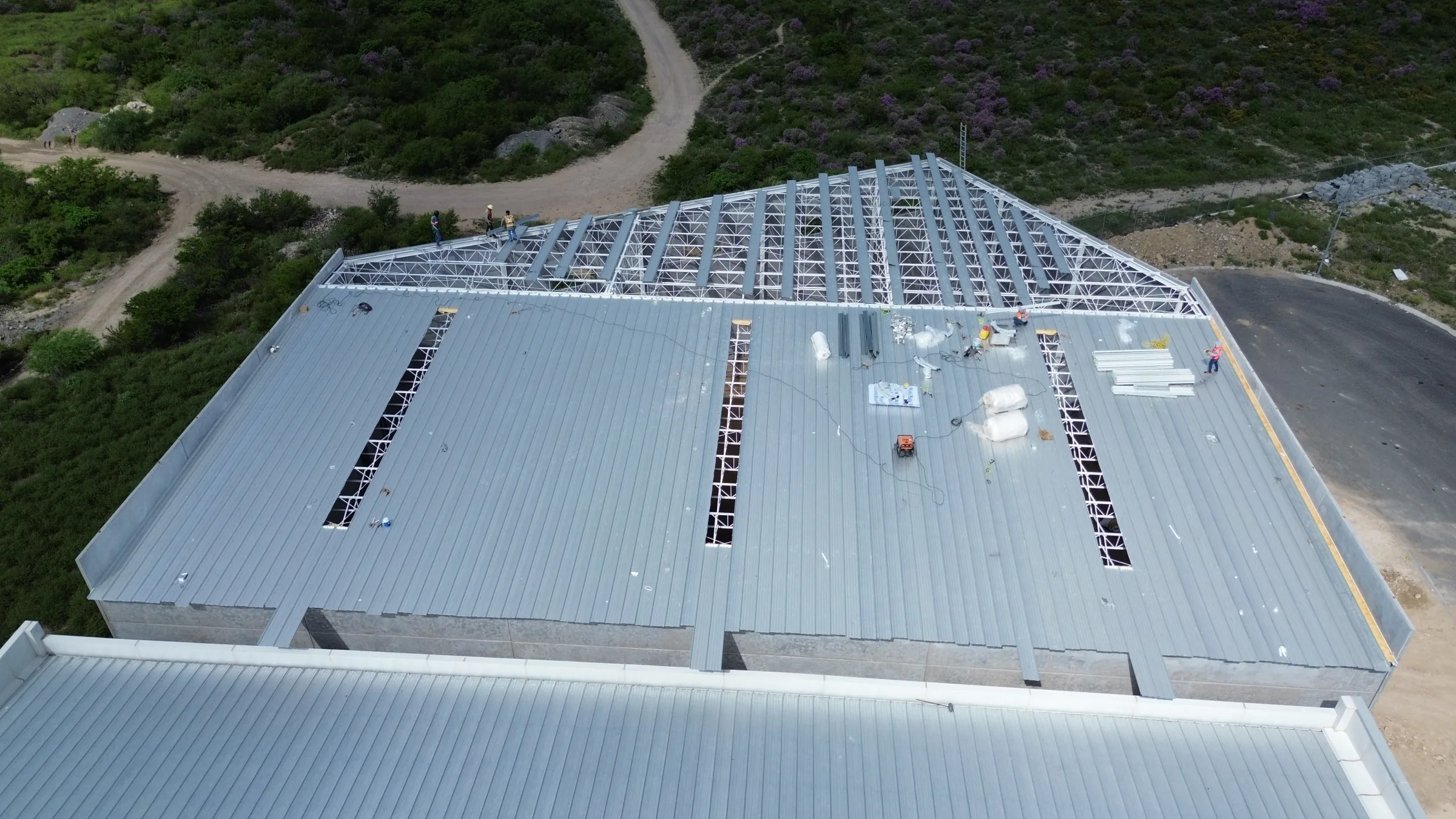 Vista cenital de la estructura metálica expuesta de una nave industrial, rodeada de vegetación