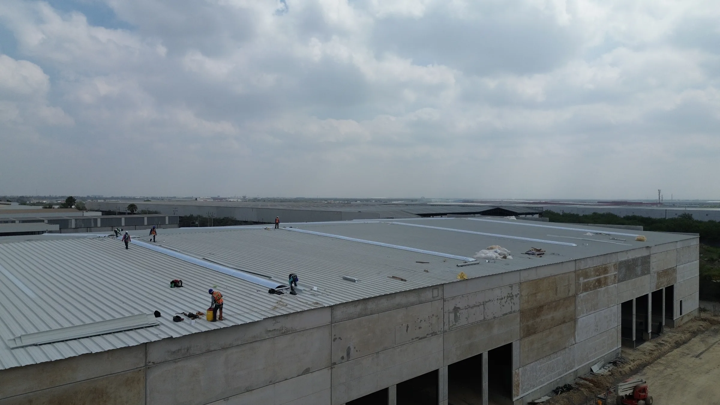 Cuadrilla instalando lámina en el techo de una nave industrial, bajo un cielo nublado